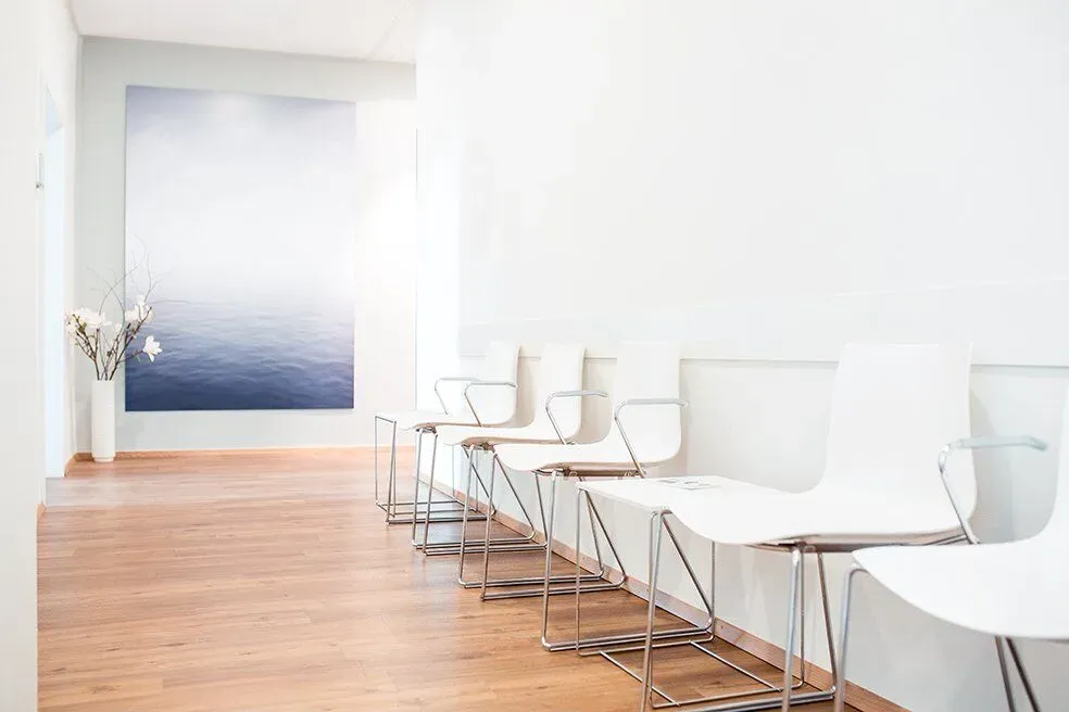 Waiting room with white chairs and a large picture of the sea