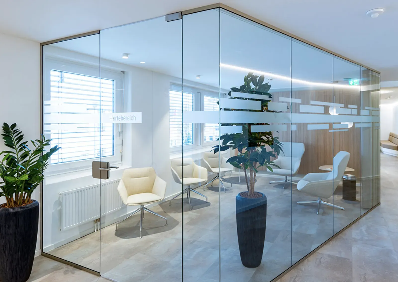 Waiting area behind glass with light armchairs and plants