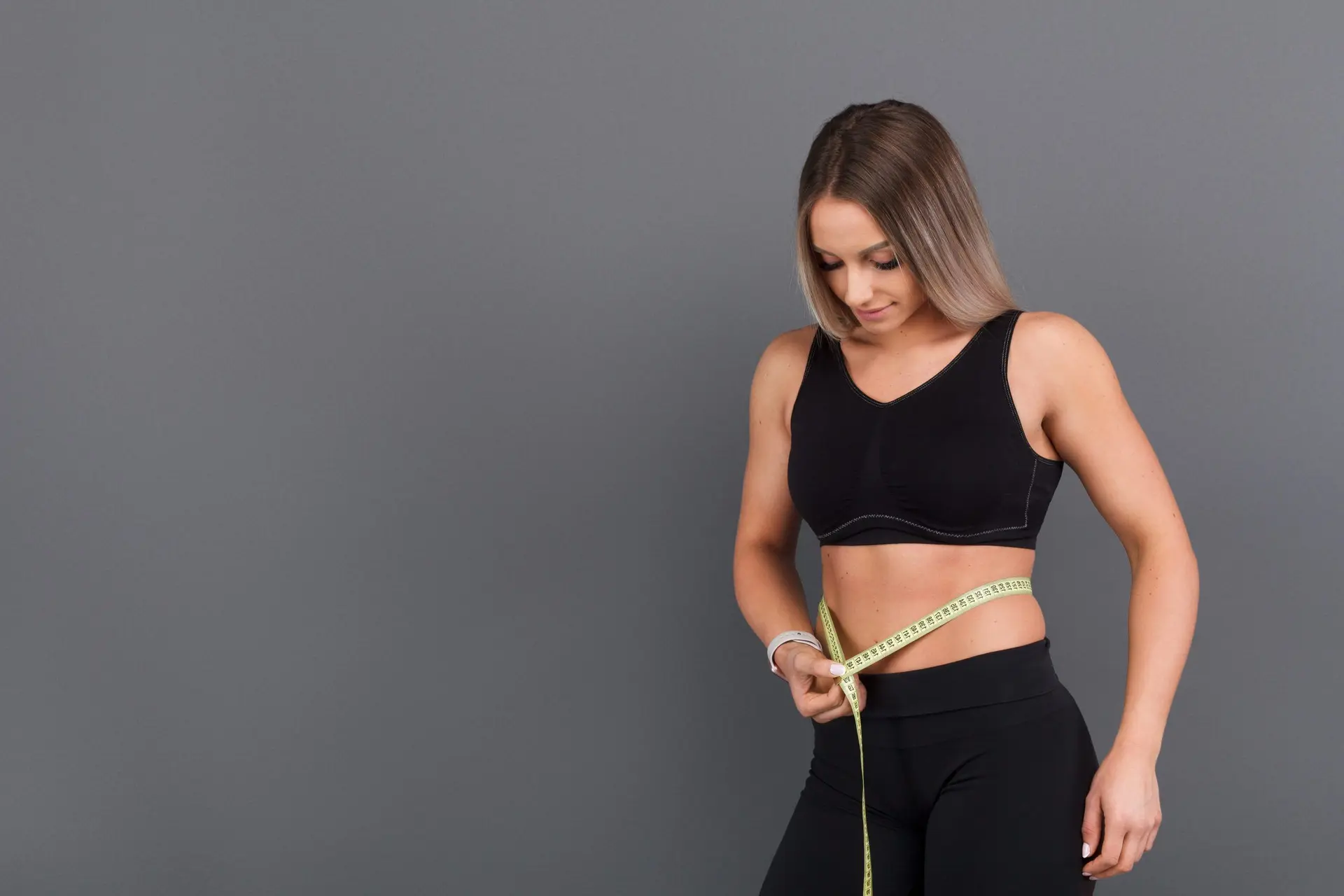 Spor kıyafetli bir kadın mezuro ile bel çevresini ölçüyor